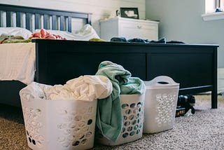 Three laundry baskets by the foot of a bed.