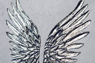 A painting of angel wings. The wings are silver and have a shiny embossed look.