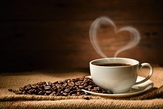 A white cup of coffee (with beans on the side) emits a heart-shaped smoke ring. Coffee reduces the risk of some cancers.