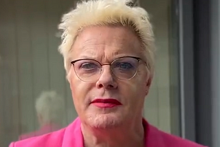 Eddie Izzard (a genderfluid person with short blonde hair and glasses wearing a pink blazer)