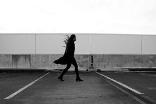 Woman walking across a carpark on a windy day.