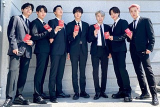 BTS lined up together in dark suits holding red diplomatic passports