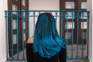 girl standing in front of gate with back turned showing teal blue hair