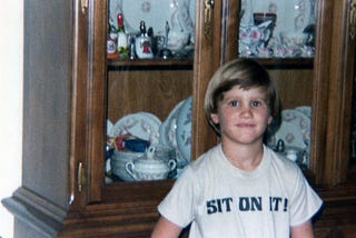 Author around age 9 wearing a shirt with iron on letters that say, “Sit on it!”