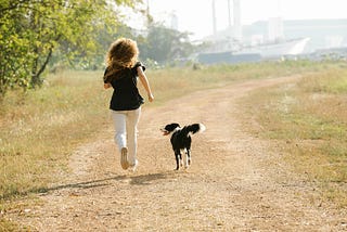 Woman running alongside a dog on a dirt trail