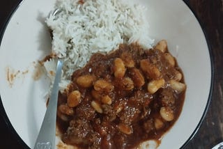 A bowl containing white rice, beef chili that appears to have been made with cannelini beans.