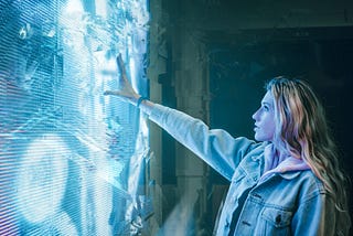 A girl faces a digital screen and reaches her hand out to it.