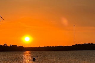 A sunset on Inks Lake outside of Austin Texas with a kayaker in the distance.