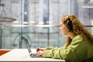 A students sits in the Laidlaw Library and works on their laptop whilst lisitening to music through headphones.