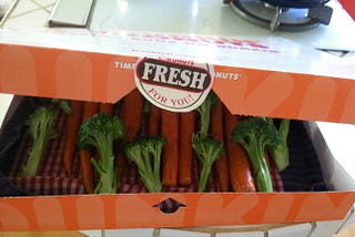 Dunkin Donuts box filled with raw carrots and broccoli.