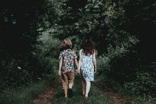 Two children walking down a forest path while holding hands
