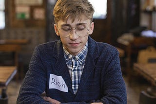 A man with the nametag Rich looking dejected as the person in front of them, at a speed dating event, is ringing the bell on the table, signalling that he should go away.