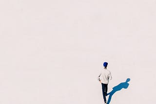 the viewpoint is from above and we can see a man walking in plain white background, his shadow is blue