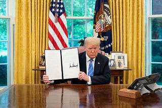 Photo of President Trump in the Oval Office holding a signed executive order