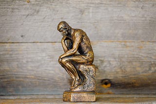 A brass man sculpture sitting with their hand on their chin slightly folded over, signifying a thinking pose.