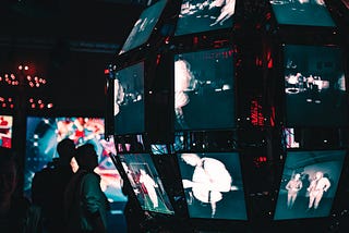 Two people look at a curved wall of monitors with different images.