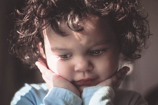 A young child holding their face with two hands under the chin