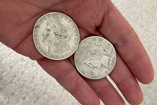 Holding two silver dollars in my hand. One is dated 1883, the other is 1922