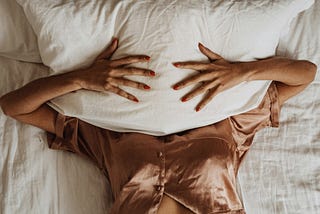 Woman lying on bed covering her face with a pillow, expressing exhaustion and frustration.
