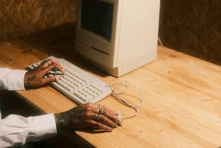 An old computer with one hand on the keyboard and one on the mouse