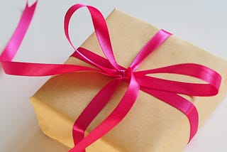 Gift box wrapped with pink ribbon, placed on a white surface.