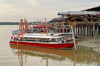 Tourist boats, covered with tarps, lined up along river. Restaurants built on stilts line the riverbank.