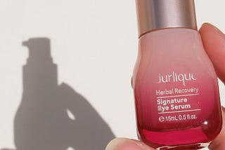 A woman’s hand holds a red bottle of Jurlique eye serum, with a shadow cast behind