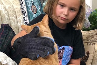 Young blonde girl using large glove to pet orange tabby cat