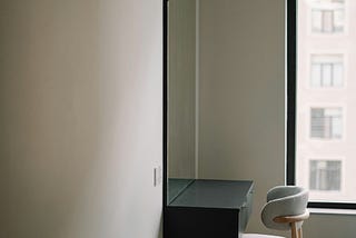 Quiet room with a simple desk and empty chair beside a window, filled with soft natural light, suggesting reflection, attention, and a slower pace of thinking