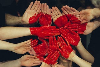 many human hands put together and painted red so they form pieces of a heart