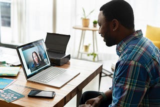 A man on a video call with a woman, smiling at his laptop