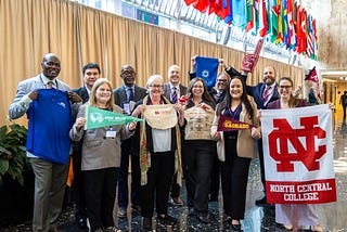 Eleven adults pose as a group while holding merchandise from the different universities they represented at the symposium.