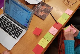 shows a wooden table top with coloured post it notes and a laptop