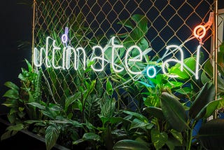 A neon sign of ultimate.ai surrounded by greenery.