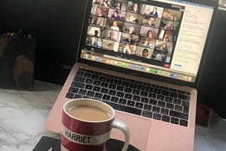 Red and white stripey mug wit the name Harriet written in black. The mug is on a black A4 notebook, next to a pencil on a desk. Behind the mug is a MacBook Air showing a Zoom screen.