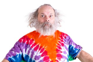 Senior man with grey hair and beard so surprised he’s wide-eyed, he is wearing a tie dye colorful t-shirt