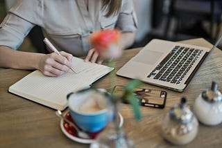 A writing desk with a computer, coffee, pen and paper