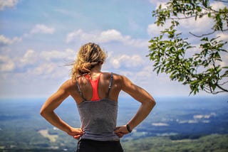 Woman standing near tree looking down across the fields below.