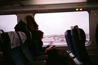 A woman sits alone on a train, reading a book.