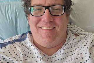 author in the hospital with a smile on his face, wires coming out of his chest, and killer curly hair