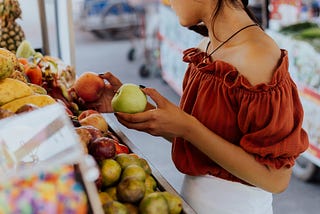 Young woman holding a green apple and an orange in the super market