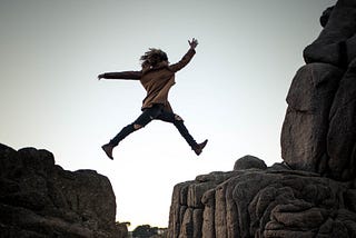 A girl jumping over a crevice on a mountain