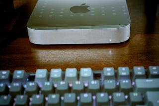 Mac mini M2 Pro (photo by author) A Mac mini sitting on a wooden desk. The top rows of a mechanical keyboard are visible in the foreground.