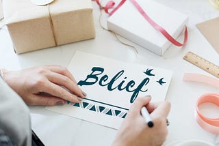 An Woman Writing belief on a white glossy paper.