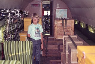 Boy (author) standing inside airplane with boxes lining one side.