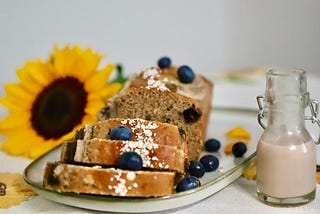 A vegan banana bread with blueberries, a glass of milk and a sunflower for decoration