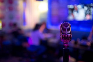 An old-fashion microphone is in the foreground, behind is an office bathed in blue light.