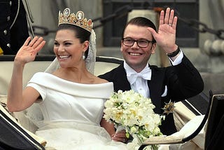 A couple in a horse-drawn carriage getting married, waving to the crowd