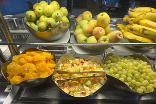 Fruit buffet at a hotel with various fresh fruits and shared tongs placed directly in the food bowls — a subtle but important food safety concern.