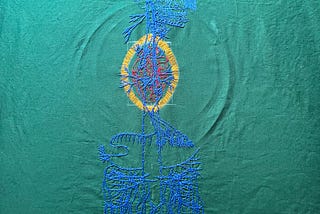 An image of an old engraving of a vagus nerve is embroidered on green cotton. The embroidery of the main nerve lines is done in blue chain stitch in perlé cotton. The brain and some of the face is stitched in the same thread in backstitch. Details in the face are stitched in single strand floss. A bright red anatomical heart is stitched in two and one strand red whipped back stitch. Around it a bright golden yellow halo in a vesica piscis shape is stitched in single strand thread.